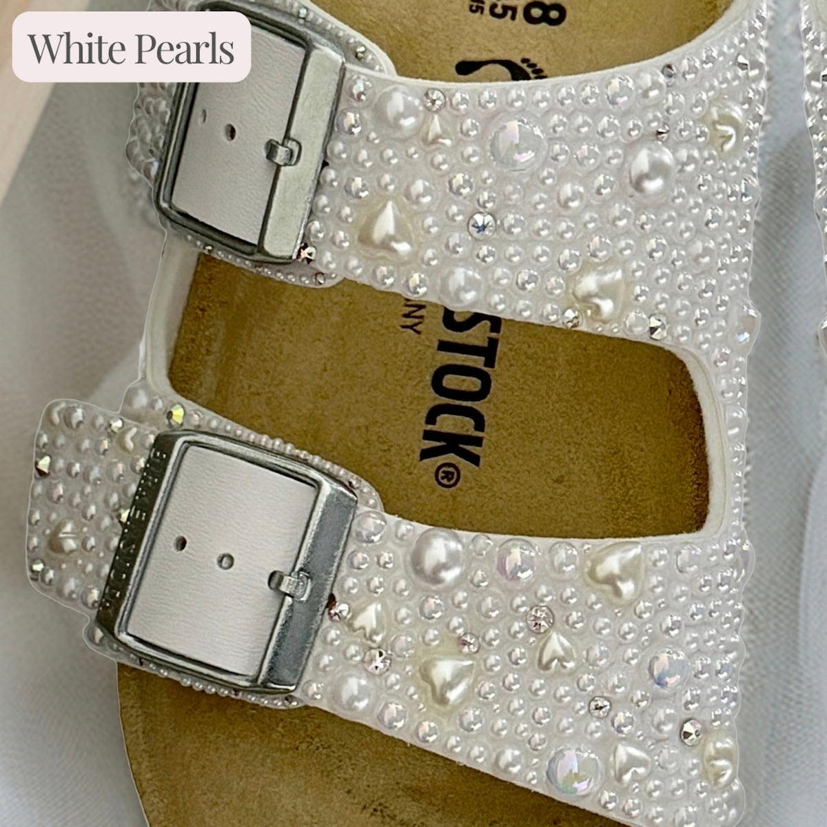 Close-up of white Birkenstock Arizona sandal straps with white pearls, delicate pearl hearts and crystal accents.