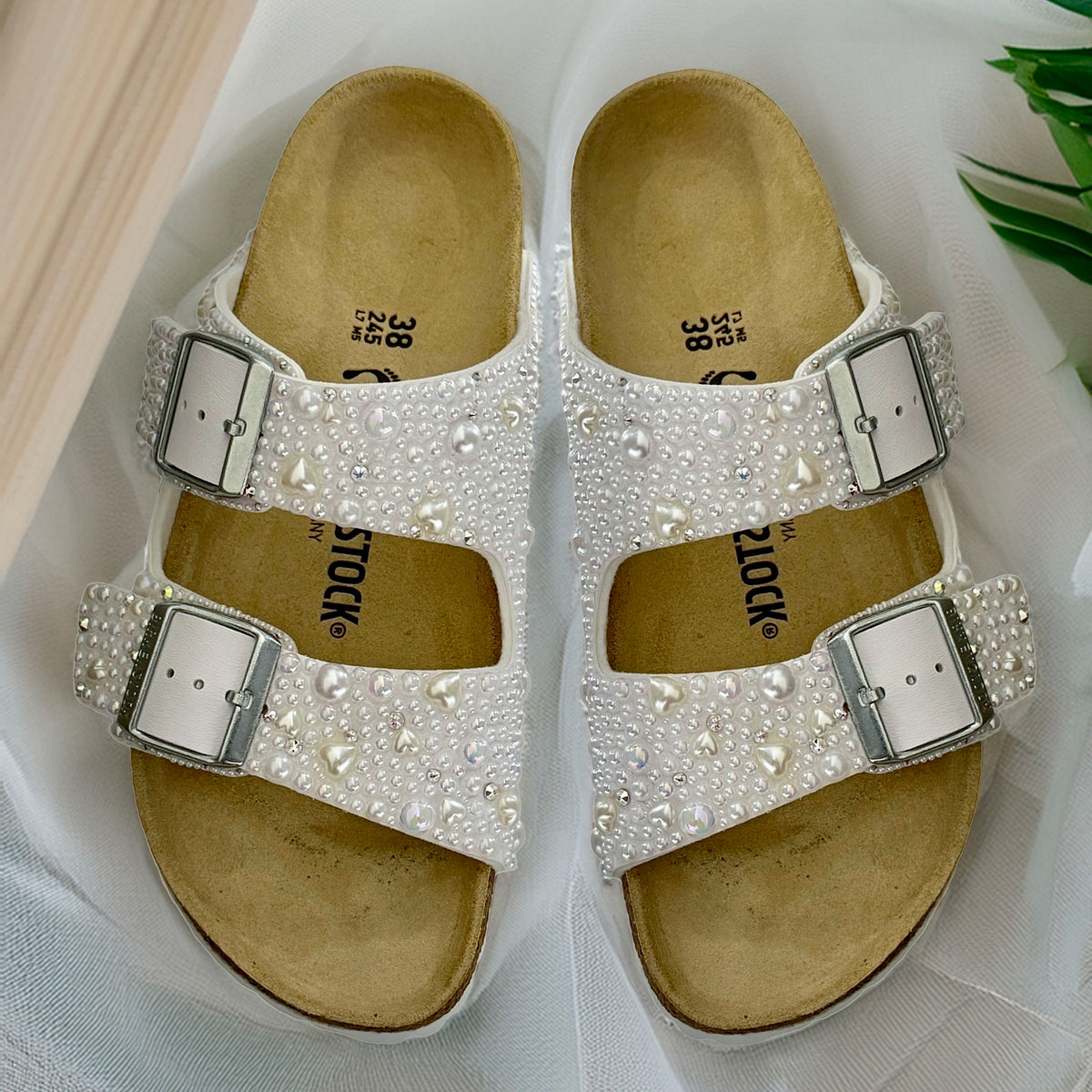 Overhead view of white Birkenstock Arizona bridal sandals with pearls, delicate pearl hearts and crystal accents on white tulle.