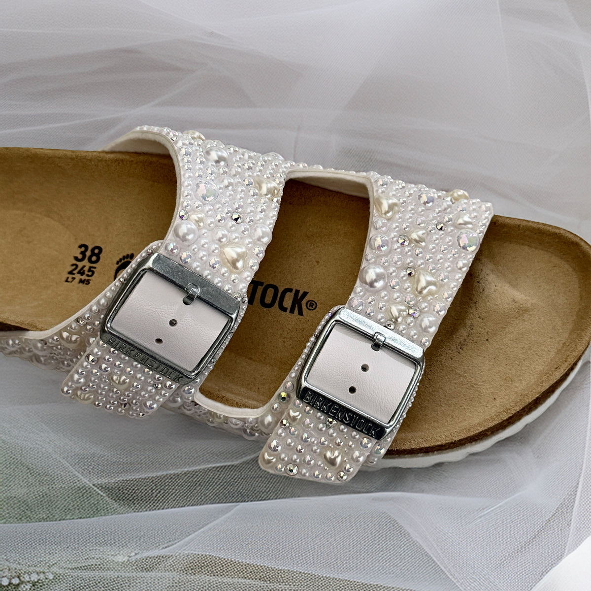 Angled view of a white Birkenstock Arizona bridal sandal with pearls, delicate pearl hearts and crystal accents across both straps.
