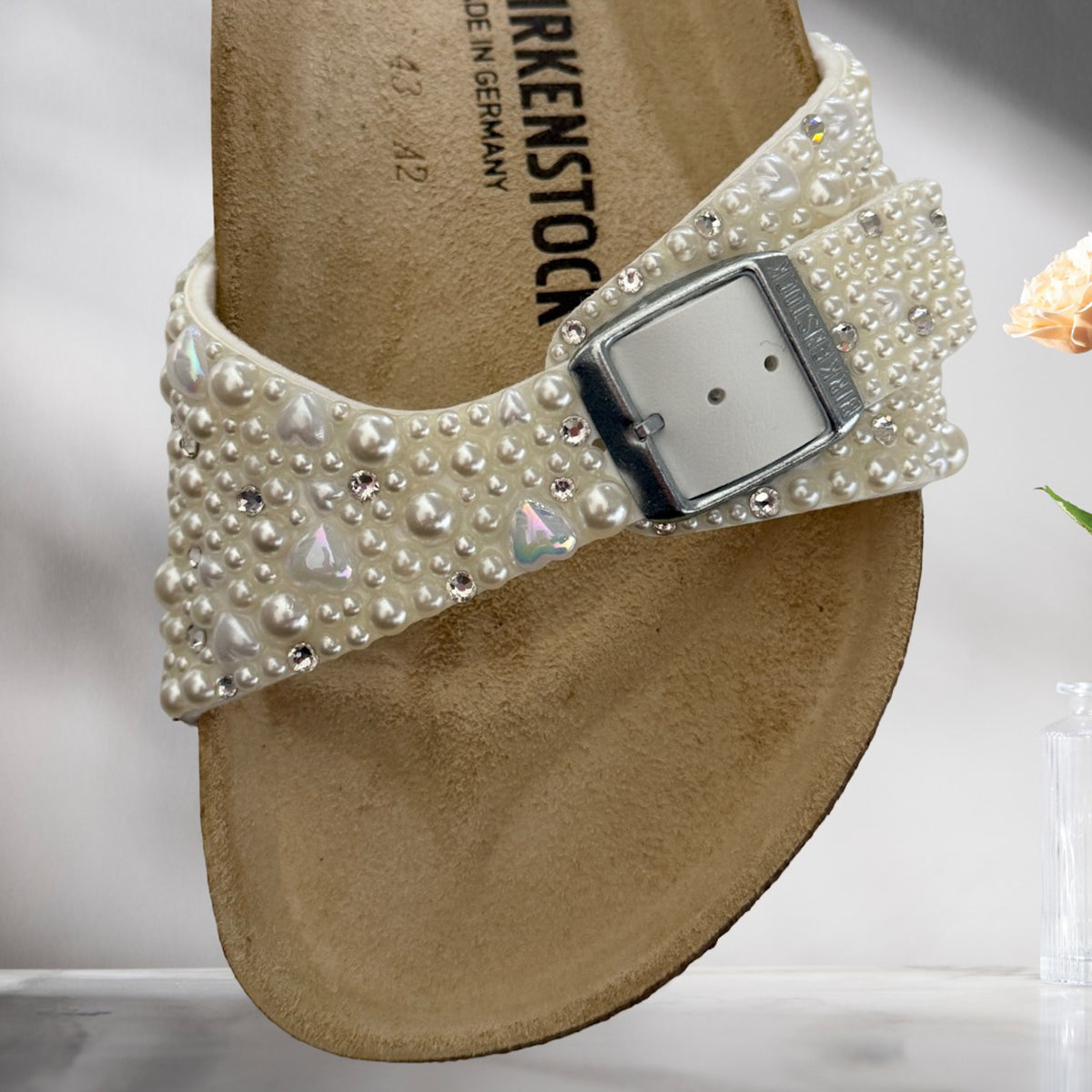 Close-up of ivory pearl detailing with delicate heart and crystal accents around the strap and silver buckle of a Birkenstock Madrid bridal sandal.